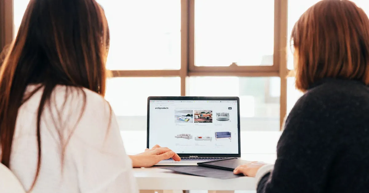 Two women use a laptop while they navigate the company's website.