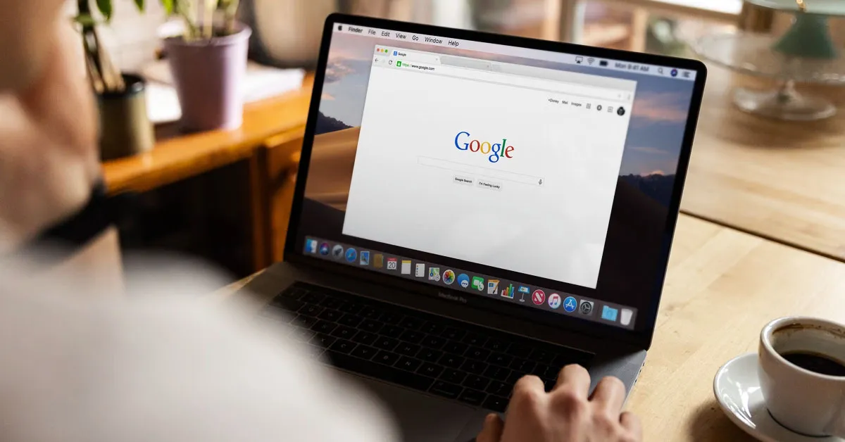 A person is using a laptop with a Google tab open. There's a coffee mug on the right side.