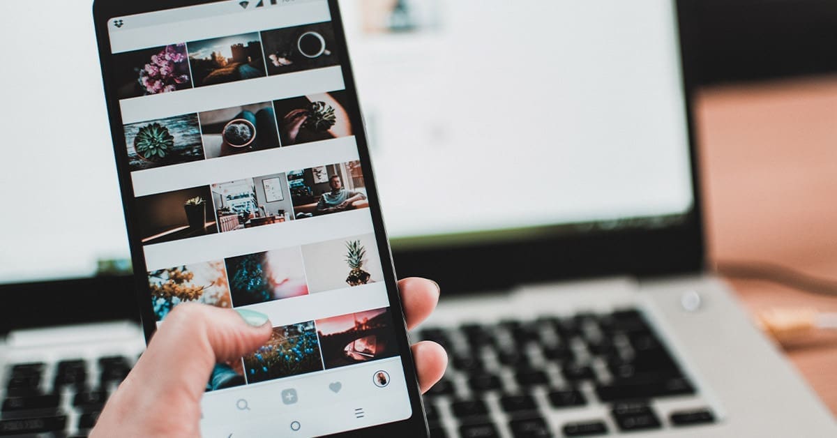 A smartphone with an Instagram feed on the screen, referring to the sales on this platform. There's a laptop in the background.