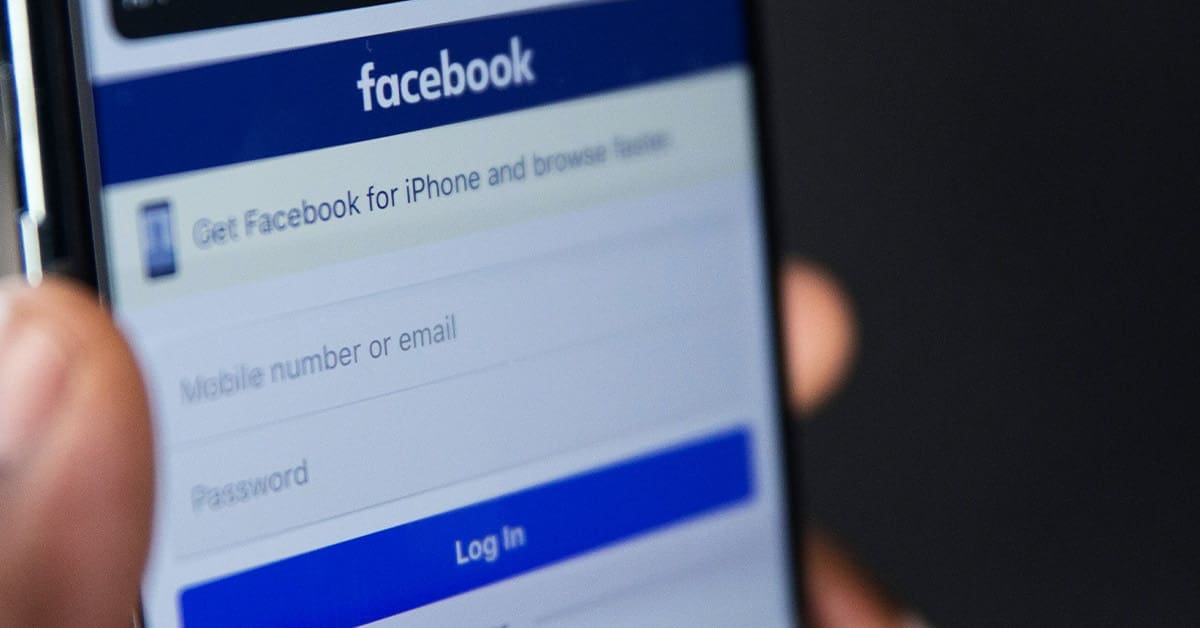 Person holding phone which shows the Facebook login screen