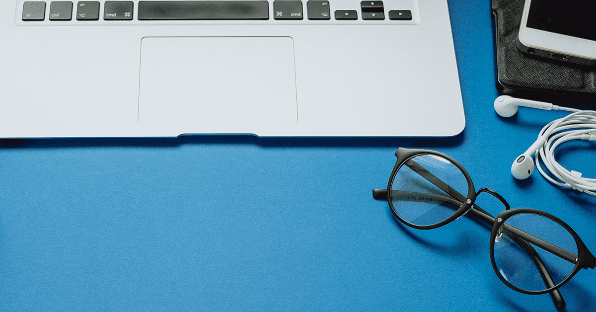 Laptop on a blue background with headphones and glasses next to it