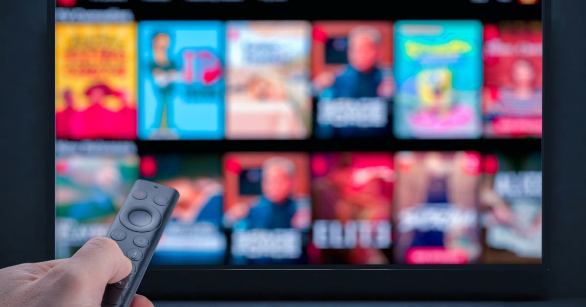 Remote control pointed at a TV that is displaying various title cards for different shows.